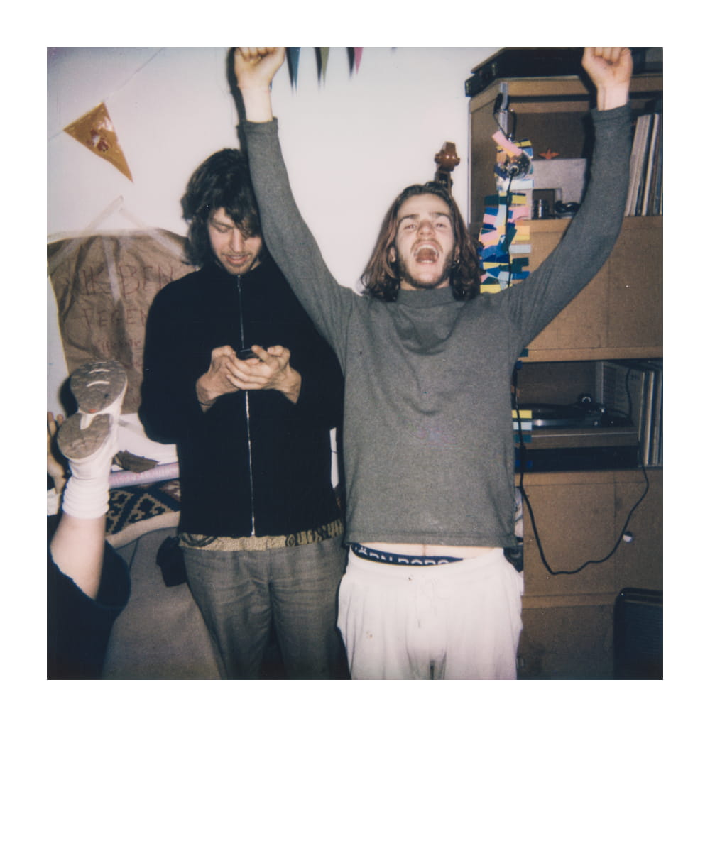 Two friends playing a tabletop RPG, one celebrating a win with raised arms and the other checking their phone.