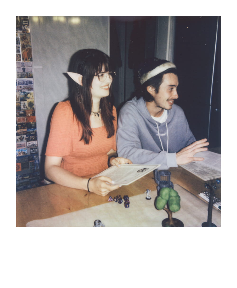 Players with elven ears and a wizard hat role-playing at a D&D session, with miniatures arranged on the table for storytelling.