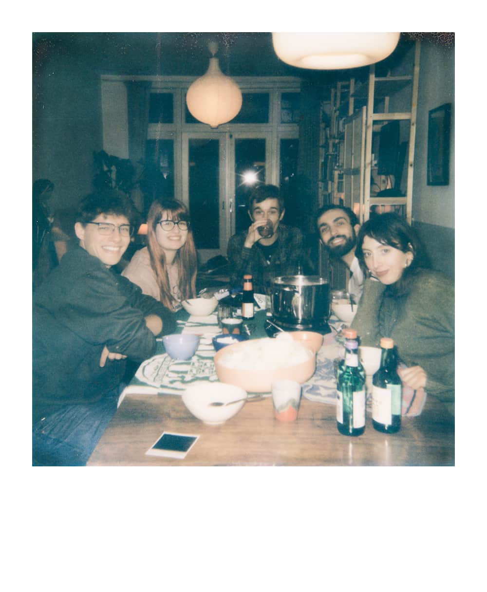 Five friends gathered in a comfy lounge room around a table with maps and drinks during a tabletop RPG session.