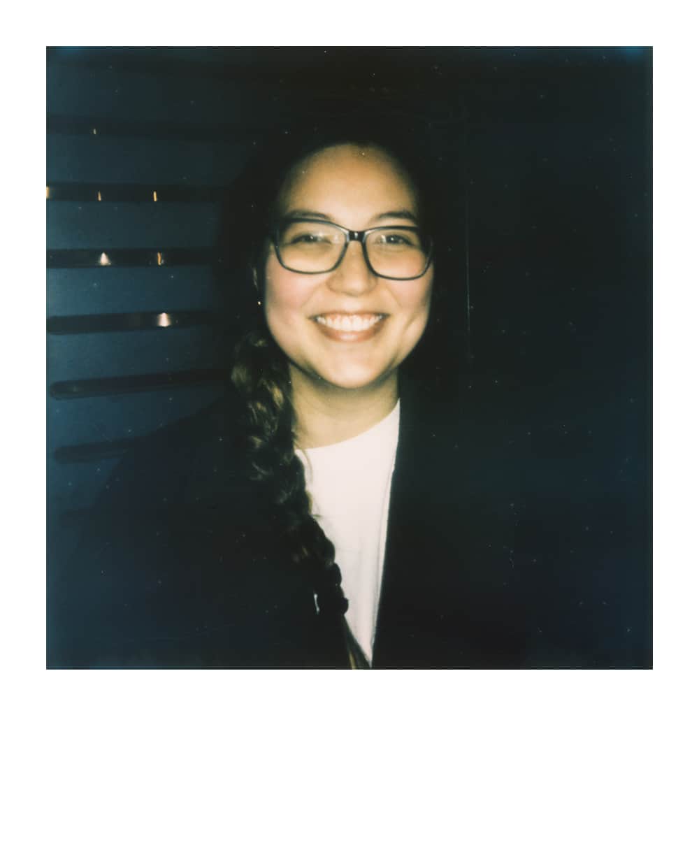 Smiling female Dungeon Master wearing glasses and who has a braid in a Polaroid-style portrait